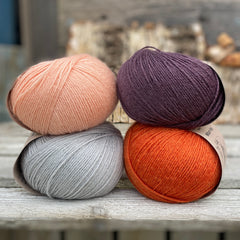 Four balls of yarn. Colours are pale blue, peach, orange and dark purple