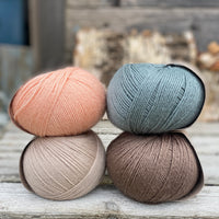 Four balls of yarn. Colours are beige, peachy orange, teal and brown