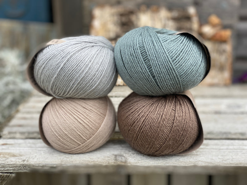 Four balls of yarn. Colours are beige, brown, teal and pale blue
