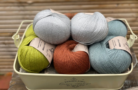 Eight balls of yarn in four pairs. From left to right the colourways are green, red-brown and blue-green with light blue sat on top