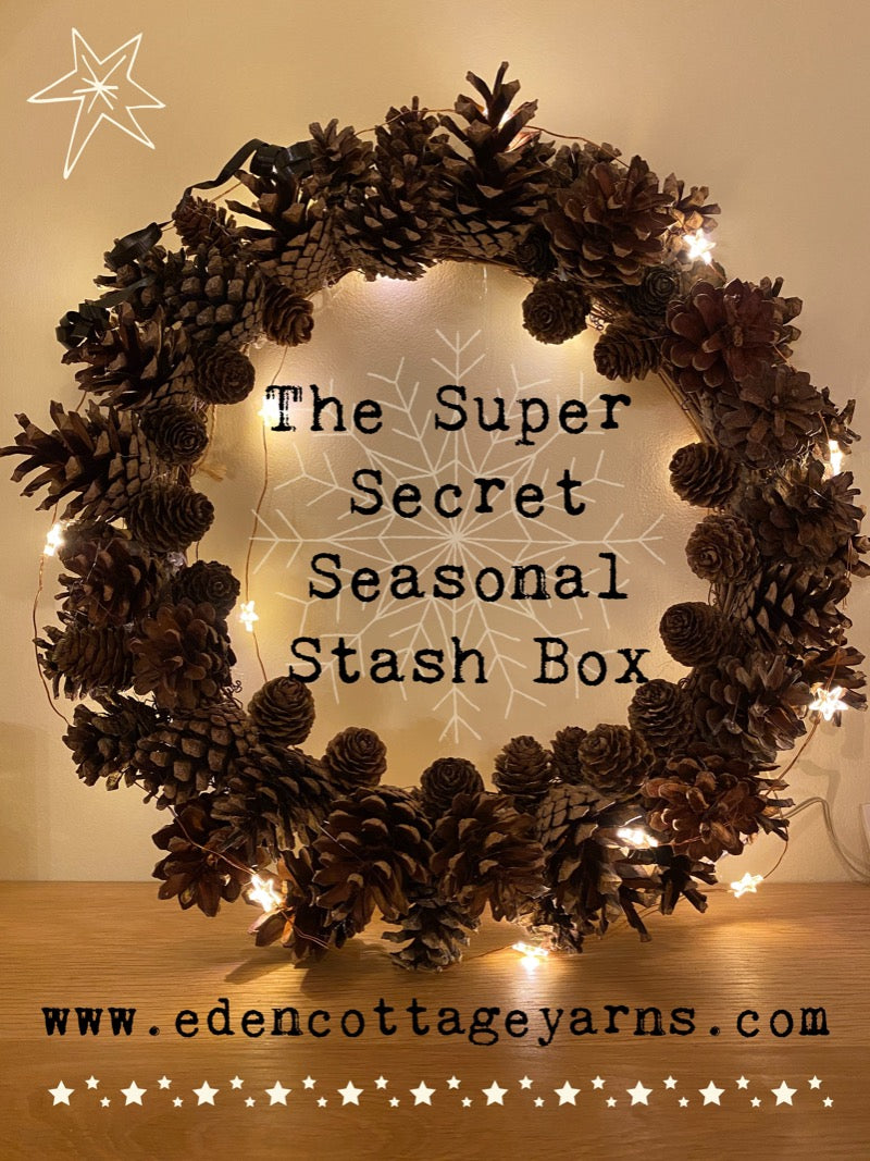 A wreath of pine cones and fairy lights, with text in the centre saying The Super Secret Seasonal Stash Box, and text below saying www.ededncottageyarns.com