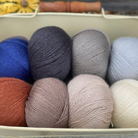 Eight balls of Milburn 4ply in shades of brown and grey with pops of red and blue