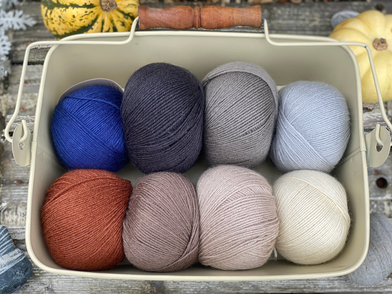 Eight balls of Milburn 4ply in shades of brown and grey with pops of red and blue