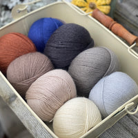 Eight balls of Milburn 4ply in shades of brown and grey with pops of red and blue