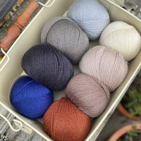 Eight balls of Milburn 4ply in shades of brown and grey with pops of red and blue