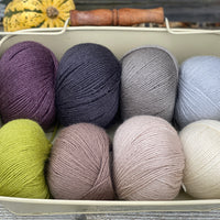 Eight balls of Milburn 4ply in shades of brown and grey with pops of purple and green 