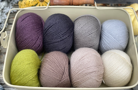 Eight balls of Milburn 4ply in shades of brown and grey with pops of purple and green 