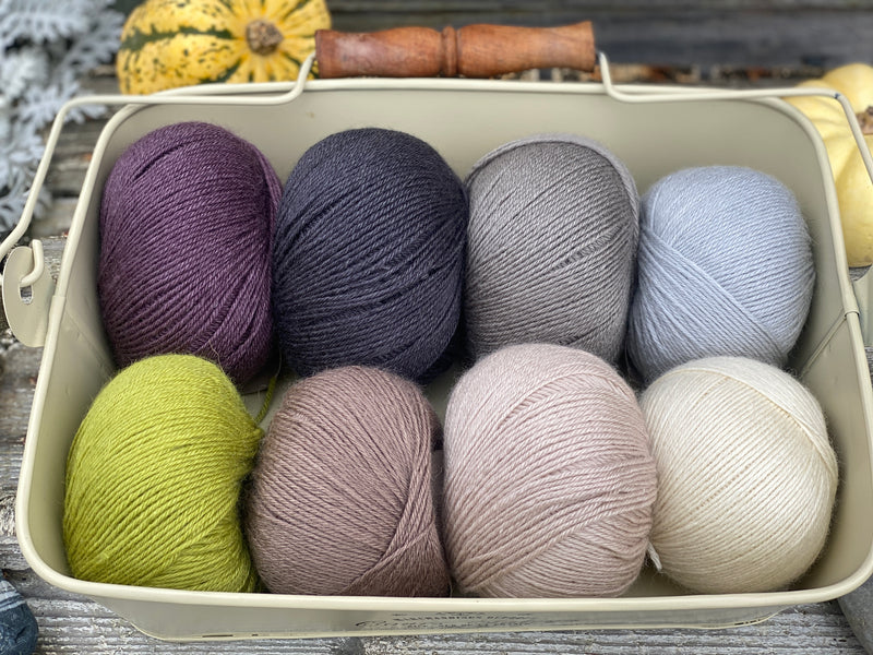Eight balls of Milburn 4ply in shades of brown and grey with pops of purple and green