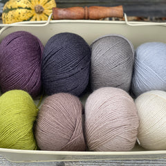 Eight balls of Milburn 4ply in shades of brown and grey with pops of purple and green