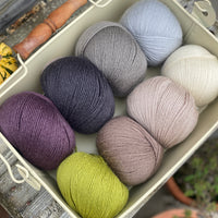 Eight balls of Milburn 4ply in shades of brown and grey with pops of purple and green