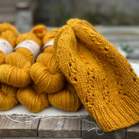 A pile of skeins of rich yellow yarn with a hat knitted in the same colourway