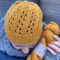 Victoria wearing a hat knitted in the same rich yellow colourway as the skein in her hand