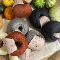 Eight balls of yarn in four colours. The colours are cream, grey and dark grey with a contrast of reddish brown