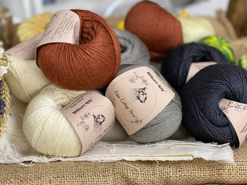 Eight balls of yarn in four colours. The colours are cream, grey and dark grey with a contrast of reddish brown