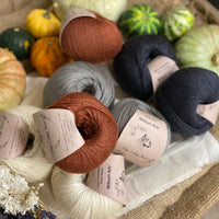 Eight balls of yarn in four colours. The colours are cream, grey and dark grey with a contrast of reddish brown