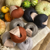 Eight balls of yarn in four colours. The colours are pale grey, mid grey and dark grey with a contrast of reddish brown