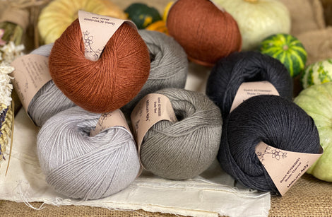 Eight balls of yarn in four colours. The colours are pale grey, mid grey and dark grey with a contrast of reddish brown