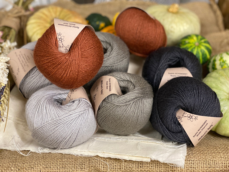Eight balls of yarn in four colours. The colours are pale grey, mid grey and dark grey with a contrast of reddish brown