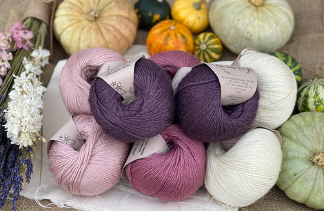 Eight balls of yarn in four colours, two each of natural cream, pale pink, dark pink and dark purple