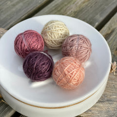 Five small balls of yarn in muted pinks and purple