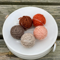 Five small balls of yarn in shades of orange and brown