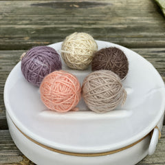 Five small balls of yarn in soft browns, purple and peach