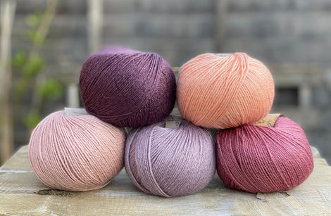 Five balls of yarn in shades of pink and purple