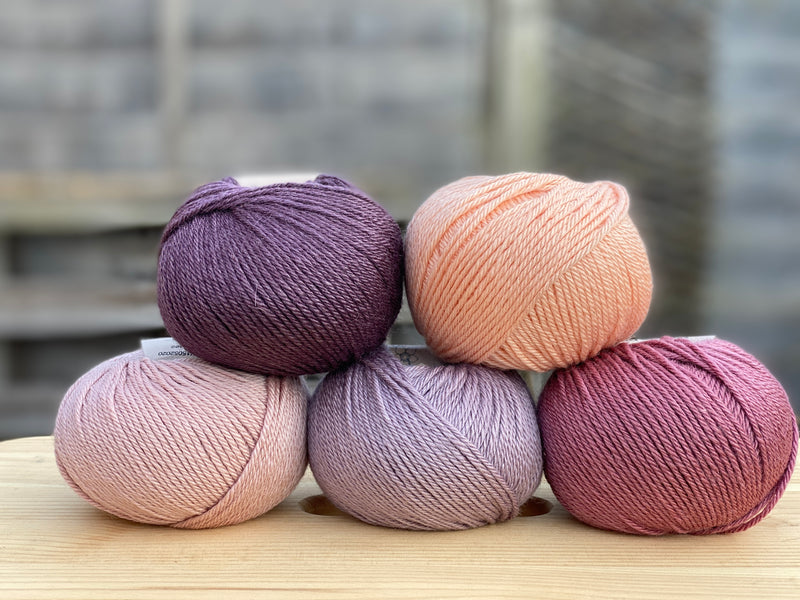 Five balls of yarn in shades of pink and purple