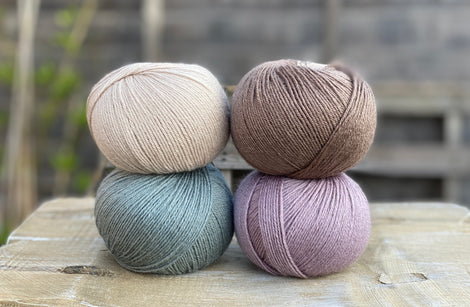 Four balls of yarn. Colours are beige, brown, teal and pale purple