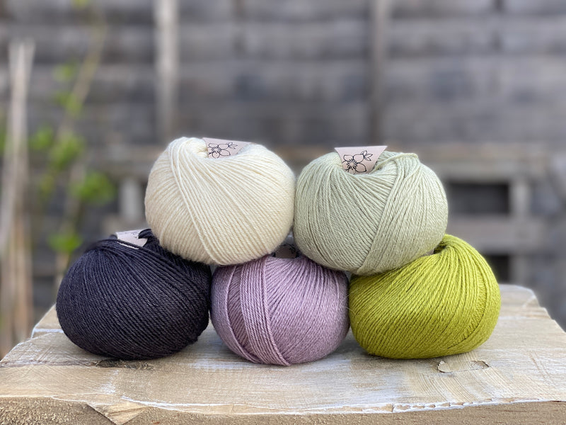 Five balls of yarn in shades of green, purple and black