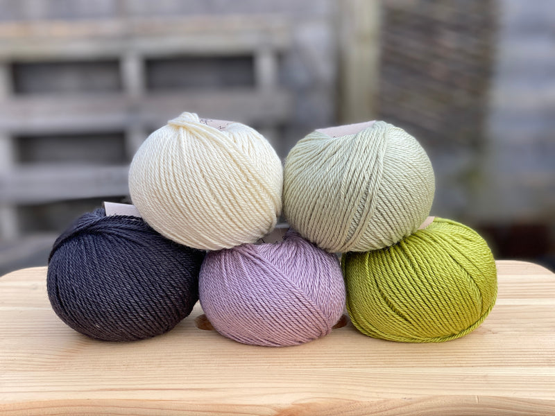 Five balls of yarn in shades of green, purple and black