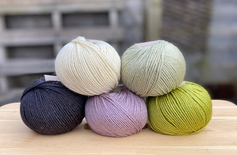 Five balls of yarn in shades of green, purple and black