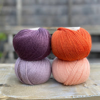 Four balls of yarn. Colours are dark purple, orange, pale purple and pale orange