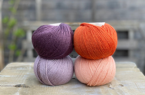 Four balls of yarn. Colours are dark purple, orange, pale purple and pale orange