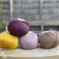 Four balls of yarn. Colours are yellow, dark purple, pale purple and brown