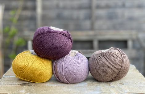 Four balls of yarn. Colours are yellow, dark purple, pale purple and brown