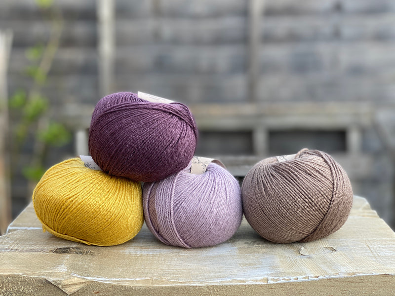 Four balls of yarn. Colours are yellow, dark purple, pale purple and brown