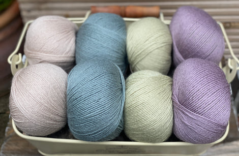 Eight balls of yarn in four pairs. From left to right the colourways are beige, blue-green, pale green, light purple