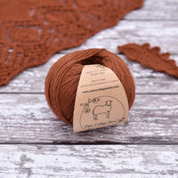 Reddish-brown yarn alongside a knitted shawl and a crochet leaf