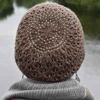 A person wearing a brown knitted hat is looking out over a lake. The hat includes a lace pattern and beads throughout