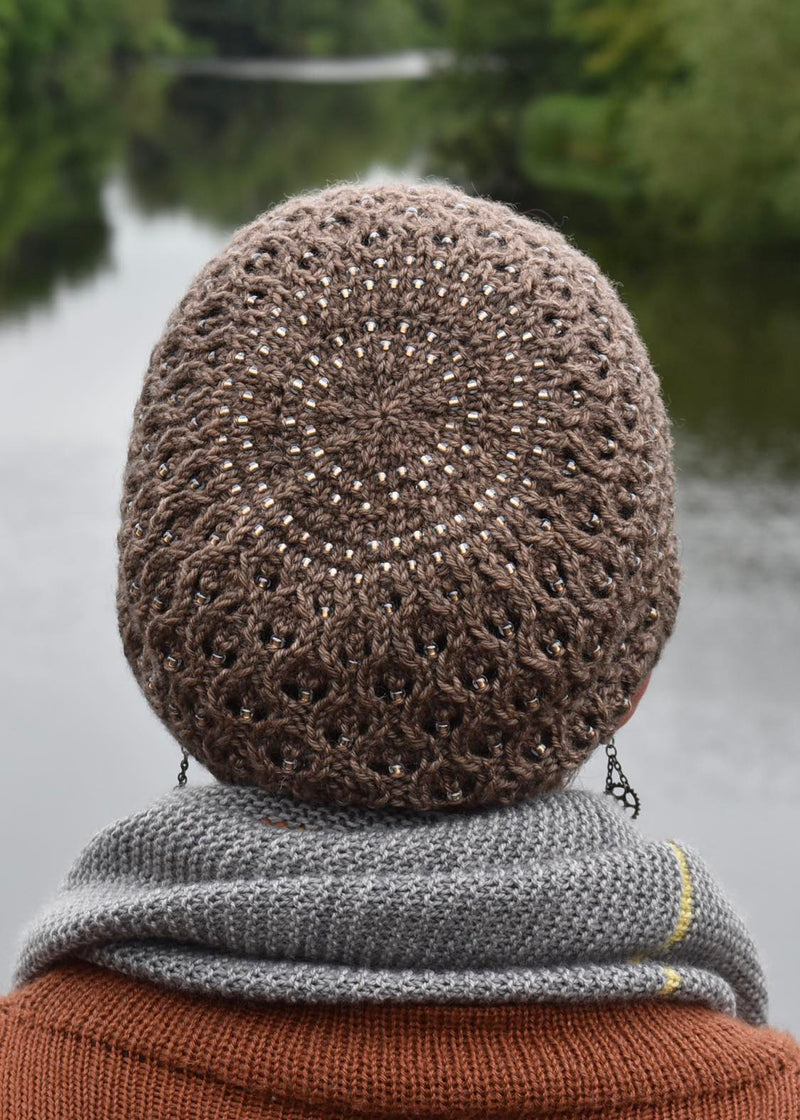 A person wearing a brown knitted hat is looking out over a lake. The hat includes a lace pattern and beads throughout