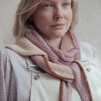 A person wearing a scarf tied like a neckerchief around their neck. The shawl is pale orange, pale purple and features an orange edging 