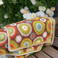 A crocheted rectangular wrap which has an all-over motif of multicoloured circles.
