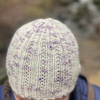 An image of Victoria's white hat with purple speckles. The hat has textured stitches running up the height of the hat and gathering at the crown