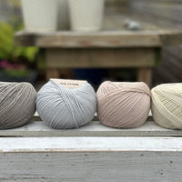 Four balls of wool in medium grey, cream, silvery grey, and oatmeal beige. 