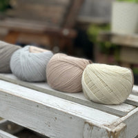 Four balls of wool in medium grey, cream, silvery grey, and oatmeal beige. 