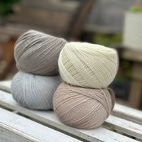 Four balls of wool in medium grey, cream, silvery grey, and oatmeal beige. 