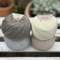 Four balls of wool in medium grey, cream, silvery grey, and oatmeal beige. 