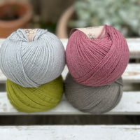 Four balls of wool in silvery grey, rich earthy lime green, medium grey, and medium soft pink. 