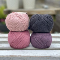 Four balls of wool in light warm pink, medium soft pink, dark aubergine purple, and dark grey. 